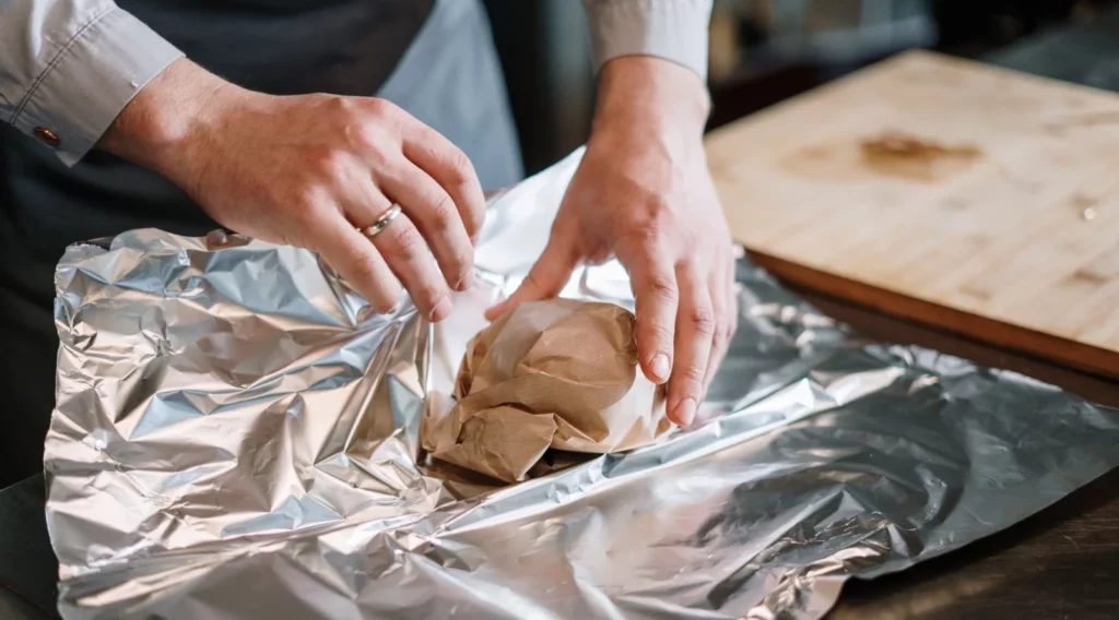 Cropped guy wrapping food with aluminium foil